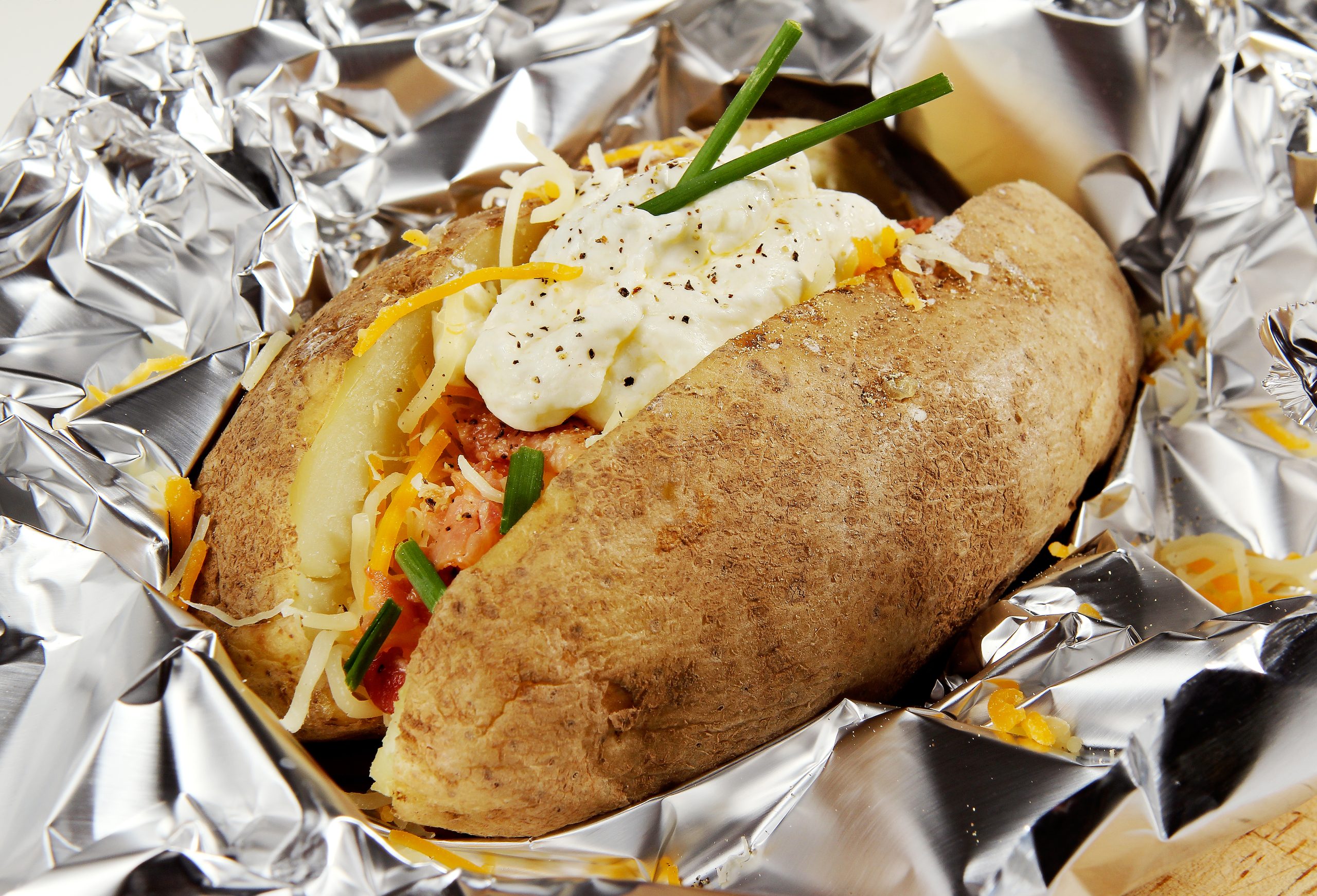 Fresh Baked Potato with Cheddar Cheese, Vegetables, Sour Cream and Chives on Aluminum Foil Food Picture