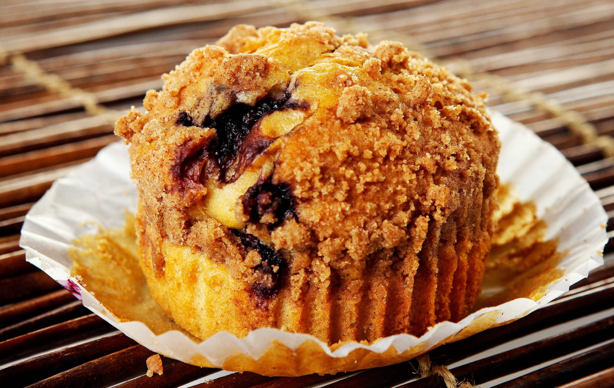 Crumbly Topped Blueberry Muffin in Wrapper on Woven Wooden Mat Food Picture