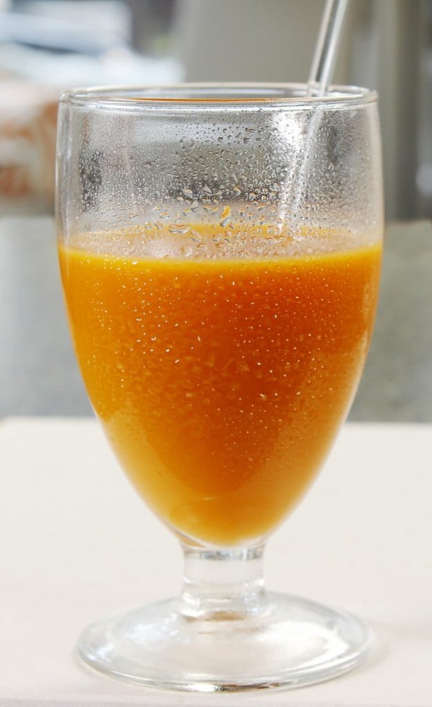 Fresh Pressed Carrot Juice in Stemmed Juice Glass with Straw on White Formica Countertop Food Picture