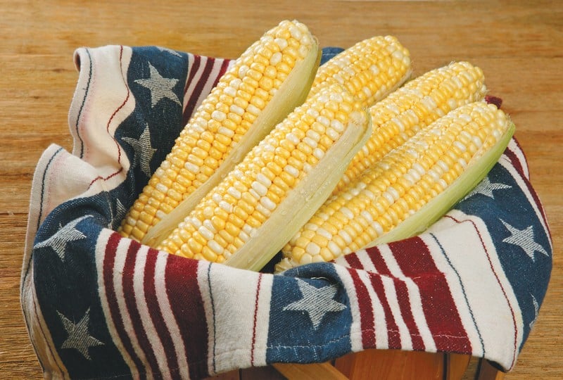 Ears of corn in basket with red, white, and blue cloth on wooden background Food Picture