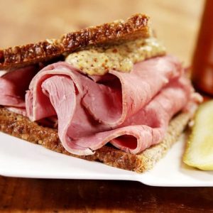 Sliced Corned Beef on Rye with Spicy Brown Mustard Sandwich with Sour Pickle on Modern White Plate Food Picture