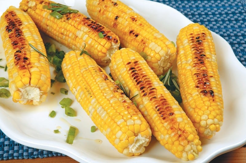 Grilled corn on the cob with garnish on a white plate and blue placemat Food Picture