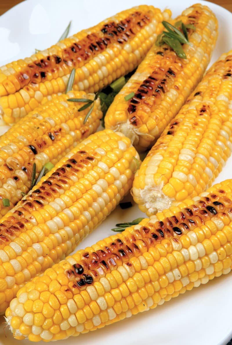 Grilled corn on the cob with garnish on a white plate Food Picture