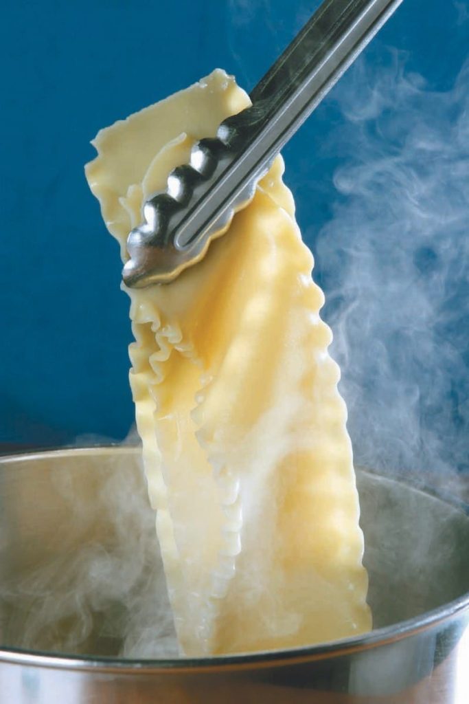 Steaming Pasta Being Held out of Pot with Tongues Food Picture