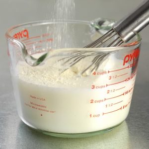 Whisked Powdered Milk in Glass Measuring Cup on Aluminum Countertop Food Picture