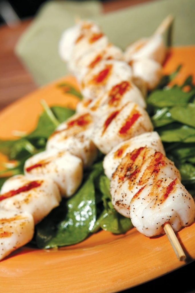 Scallops on Skewers over Greens on Orange Plate Food Picture