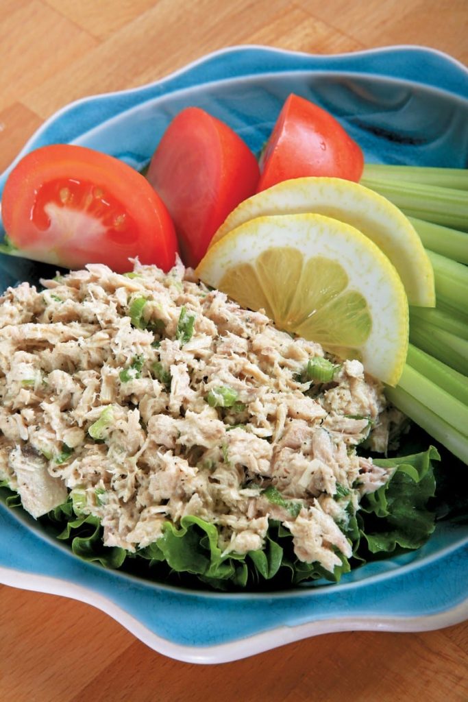 Tuna salad with veggies and garnish on blue plate with wooden surface Food Picture
